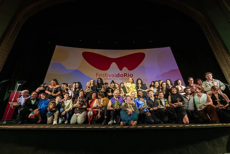 Festival do Rio winners gathered on stage with their trophies, in front of the festival sign