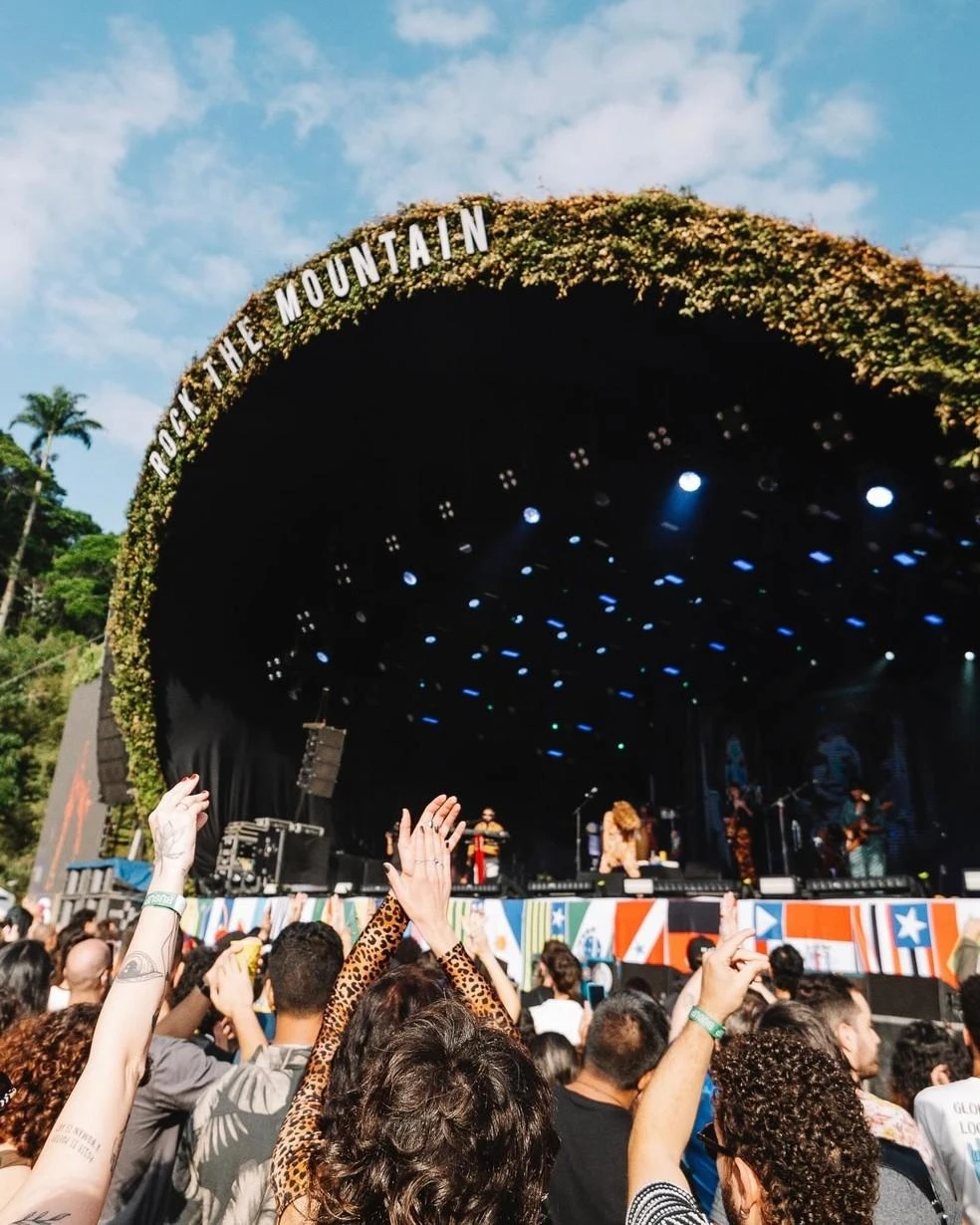 Público com as mãos para o alto diante do palco em arco coberto de folhagens do Rock the Mountain