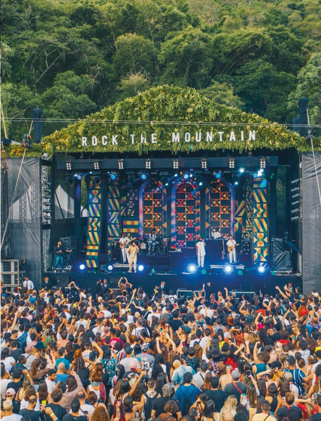 Show no palco do Rock the Mountain com cenografia de padrões coloridos, público lotado e a mata da serra ao fundo