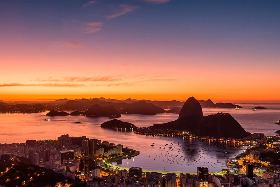 Amanhecer sobre a Baía de Guanabara, com o Pão de Açúcar e Botafogo iluminados