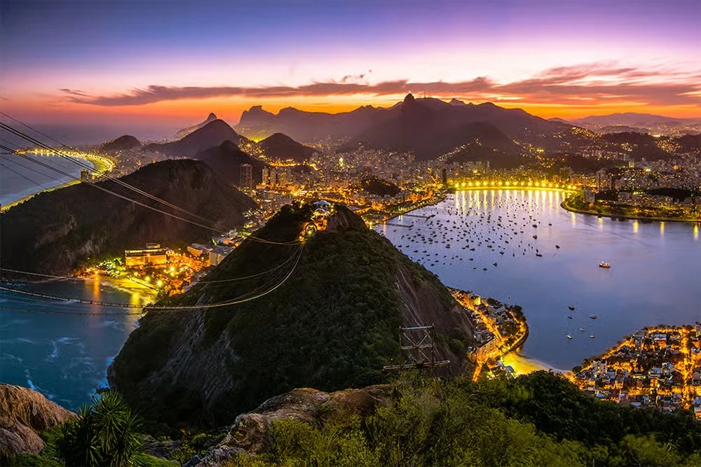 Enseada de Botafogo iluminada à noite, vista do alto com o Cristo Redentor ao fundo